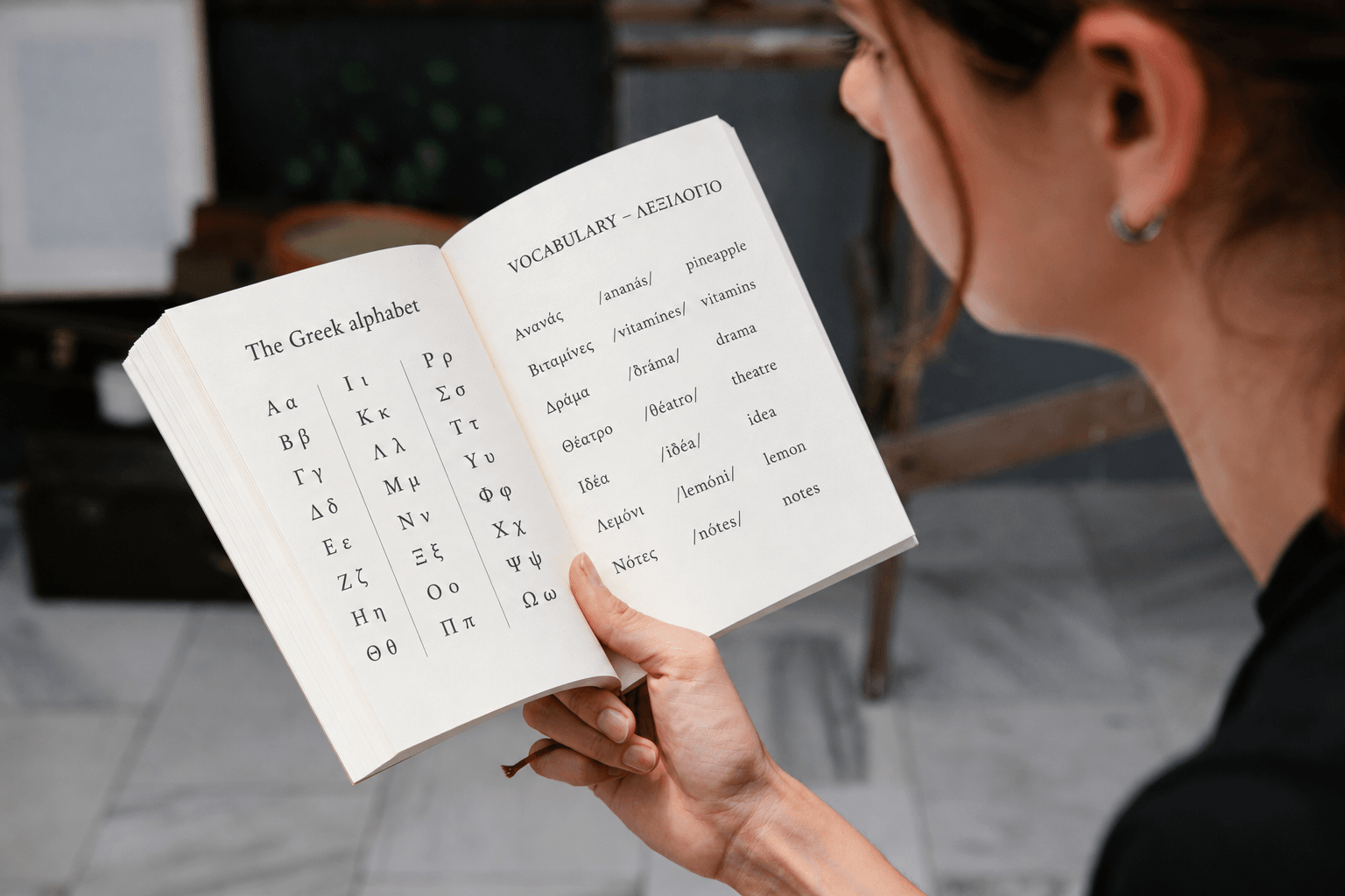 Woman reading an open book with the Greek alphabet and beginner Greek vocabulary